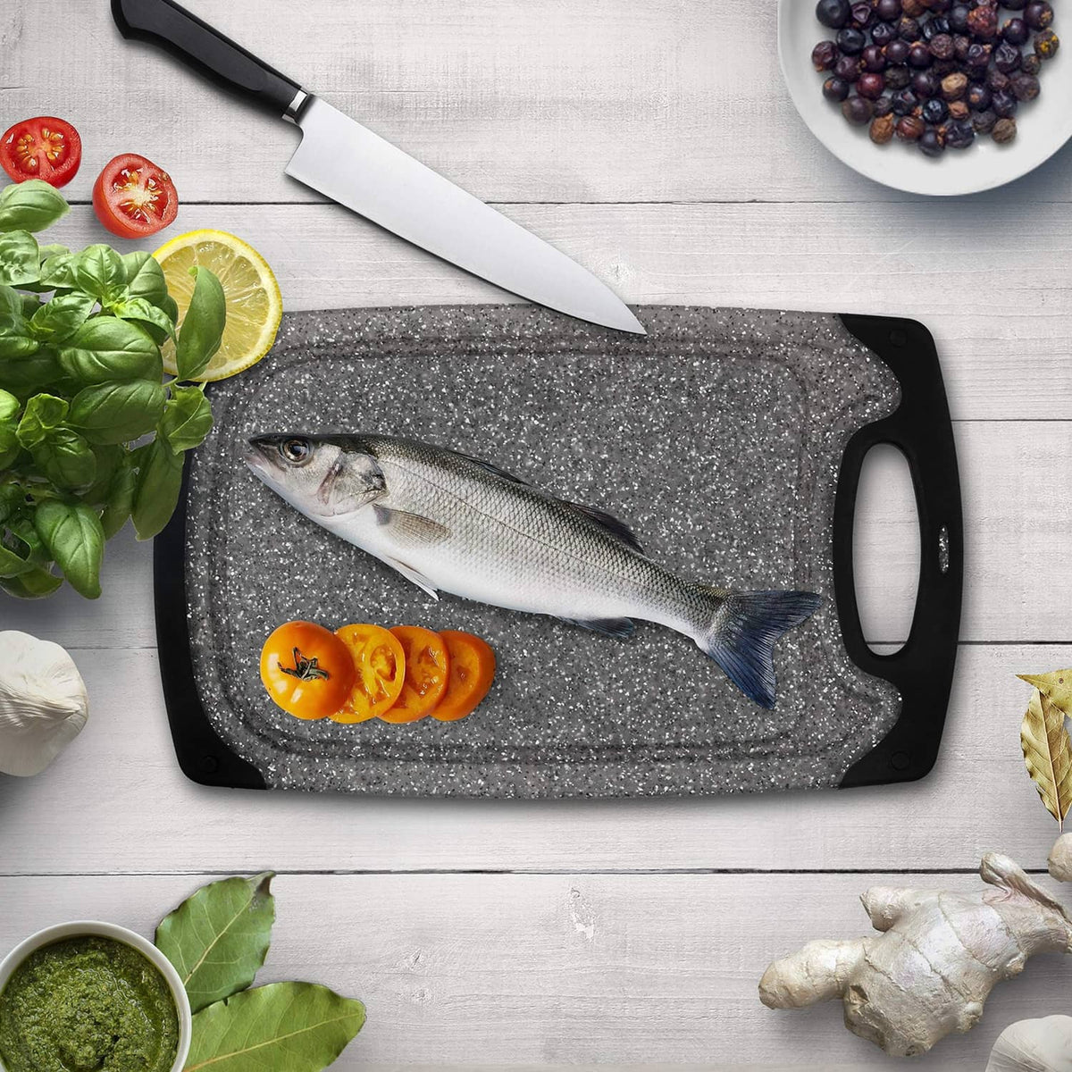 Gray speckled cutting board with black frame and handle, fish and sliced vegetables on top