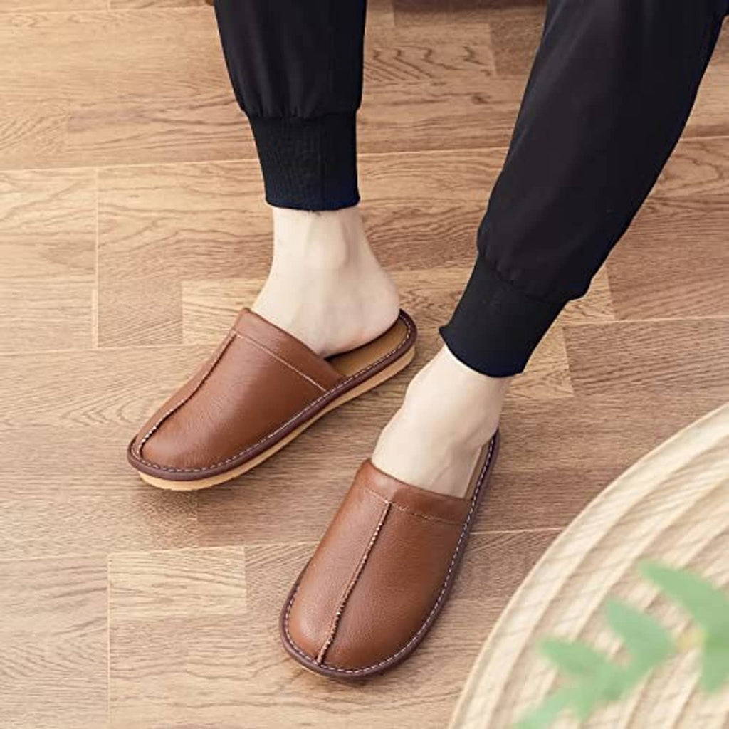 Light brown leather slip-on slippers worn with dark pants on wooden floor