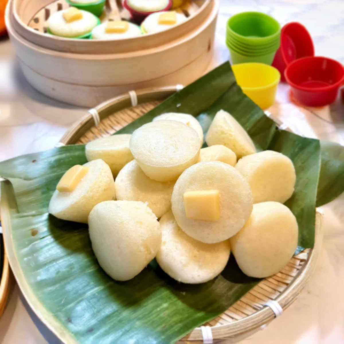 Silicone puto mold cups in red, yellow, and green beside steamed puto on banana leaves