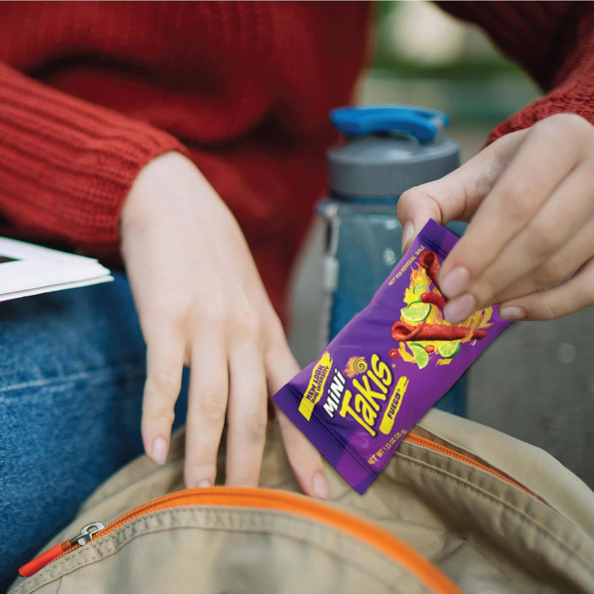 Hand holding a purple Takis Mini Fuego 25 singles snack pouch