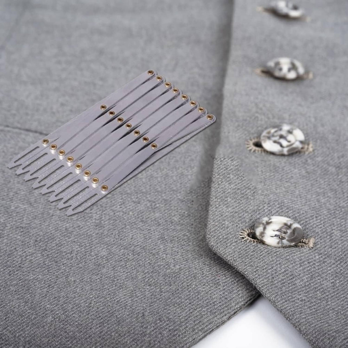 Expanding aluminum sewing gauge lying on gray fabric beside small buttons