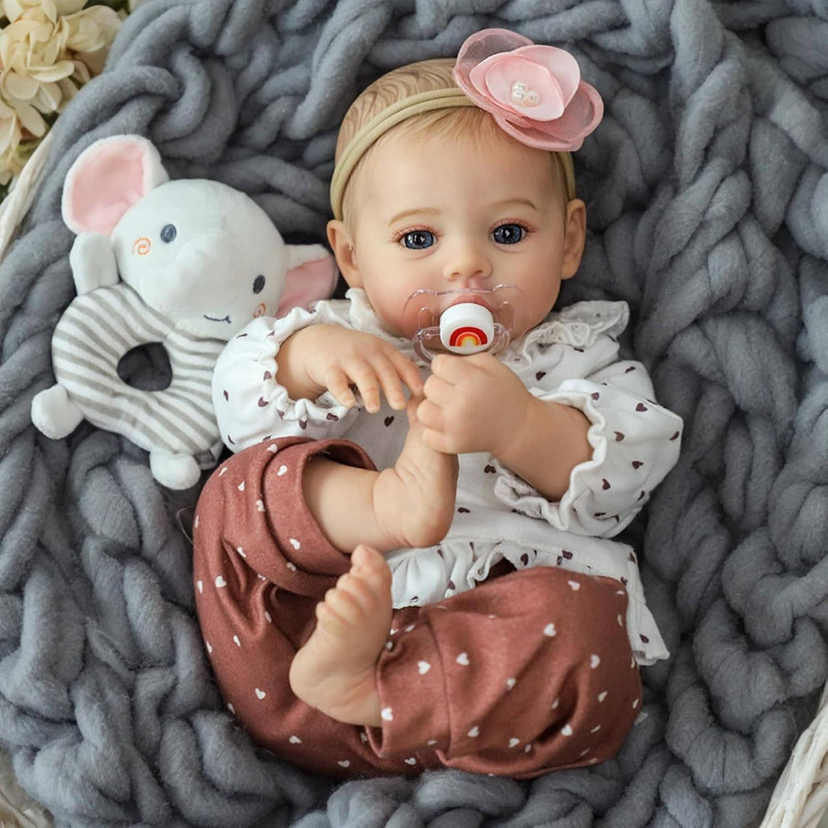 Realistic baby doll with pacifier, pink flower headband, brown patterned pants, plush bunny