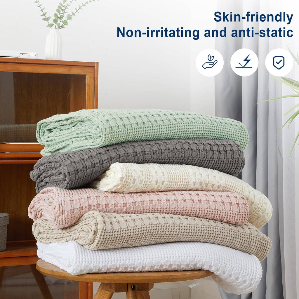 Stack of waffle-weave cotton blankets in mixed colors: green, gray, beige, and pink