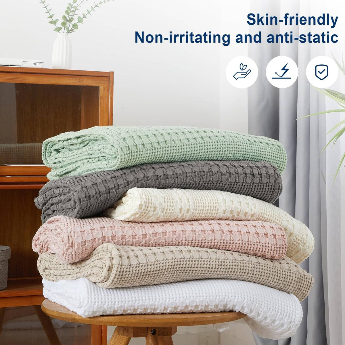 Stack of waffle-weave cotton blankets in mixed colors: green, gray, beige, and pink