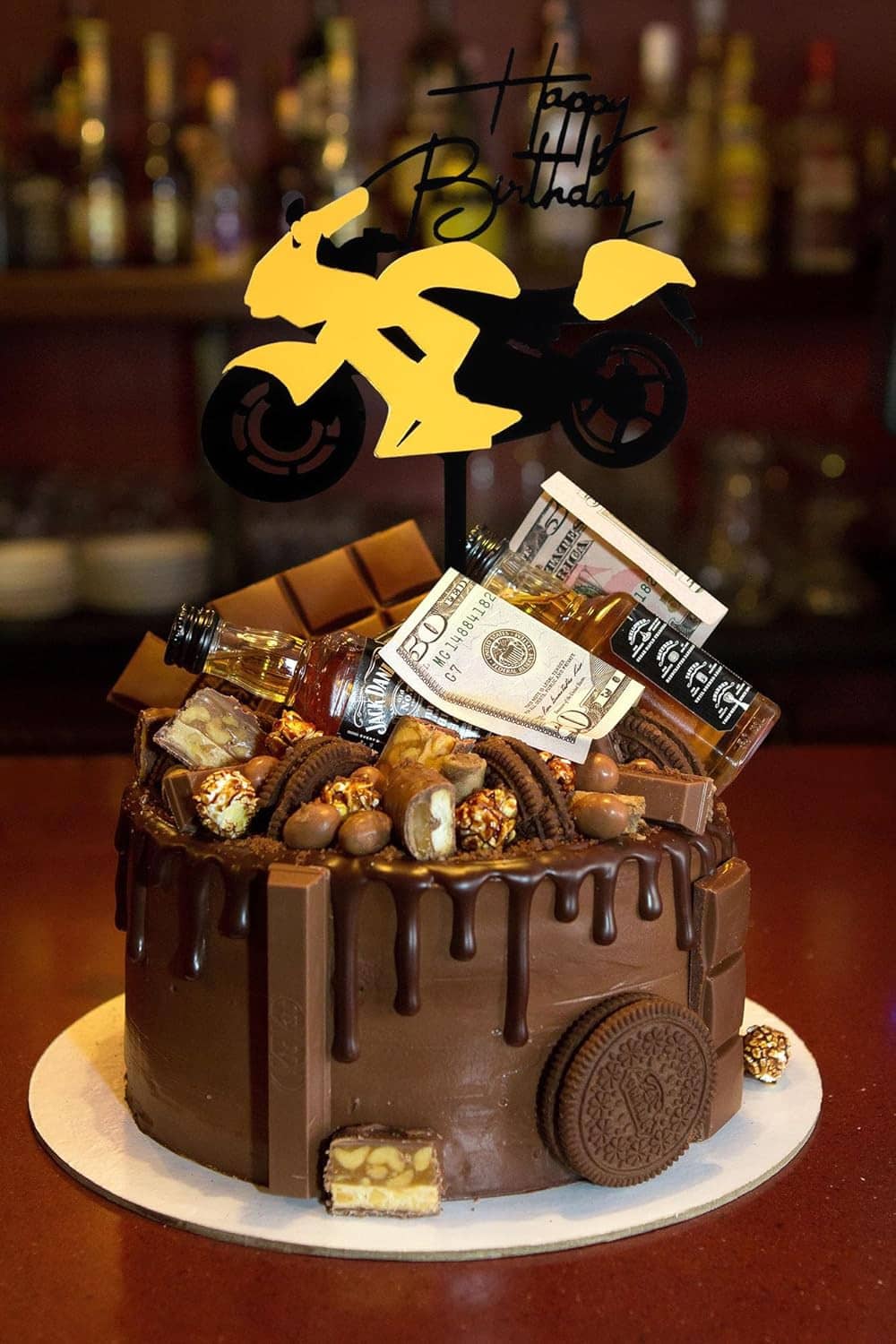 Motorcycle cake topper on a chocolate drip cake with 'Happy Birthday' text