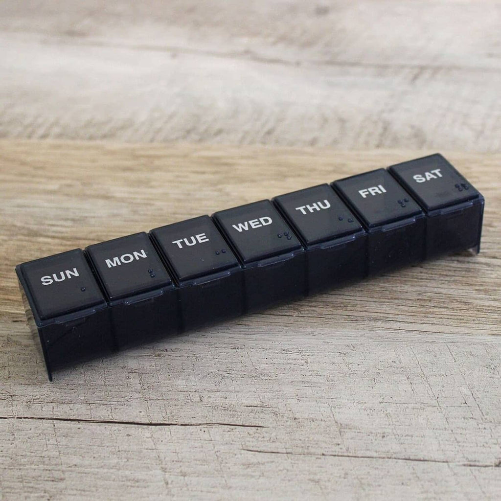 7-day pill organizer with dark Sun through Sat compartments on a wooden surface