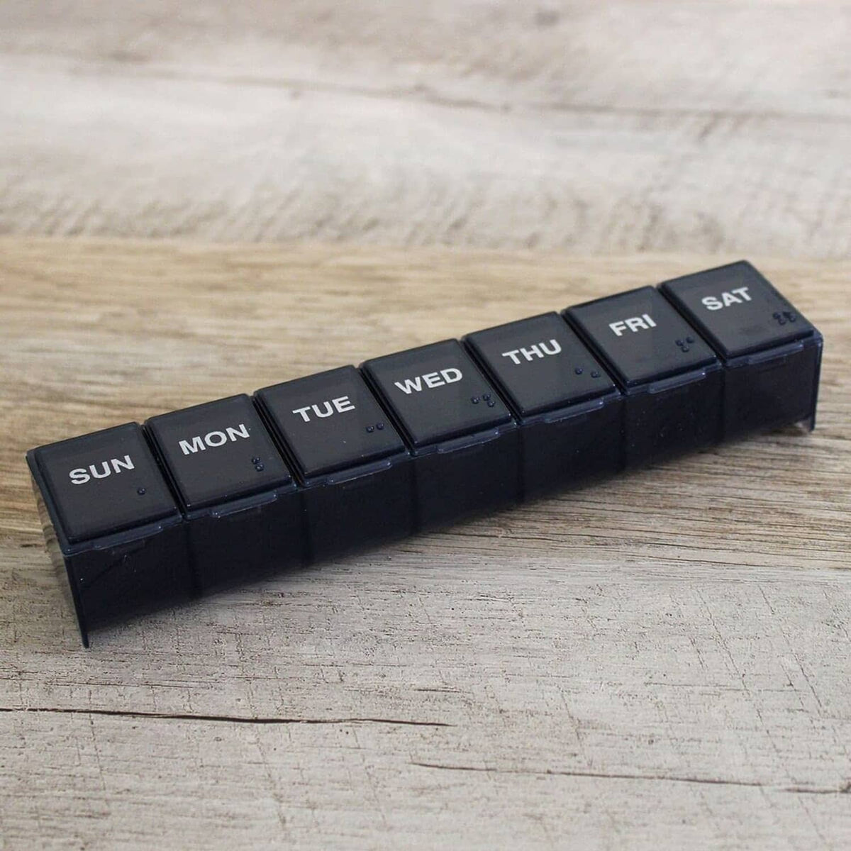 7-day pill organizer with dark Sun through Sat compartments on a wooden surface