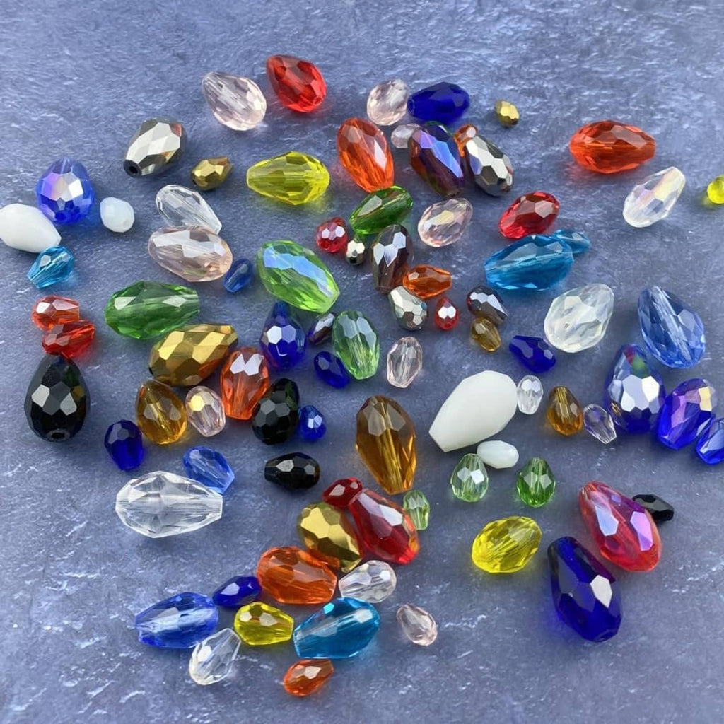Mixed-color faceted glass teardrop beads with vertical holes scattered on a surface
