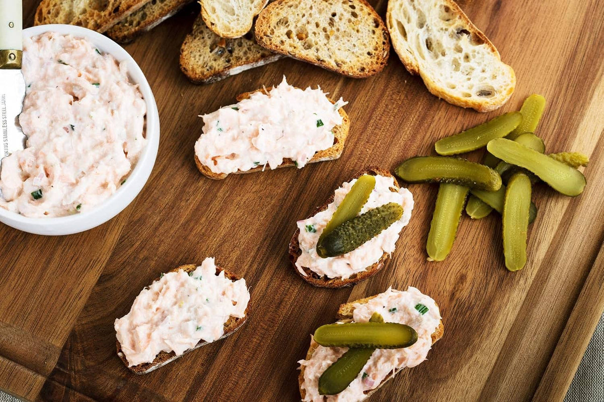 Wooden board with sliced cornichons and small bread pieces