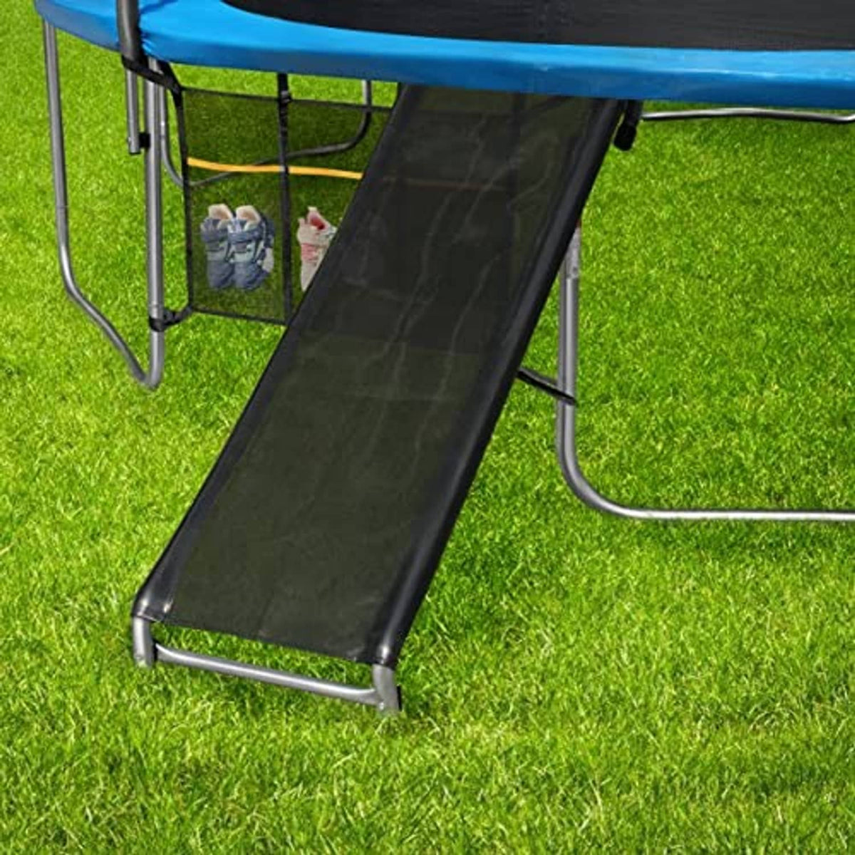 Outdoor trampoline slide ramp with black ladder and metal supports on grass