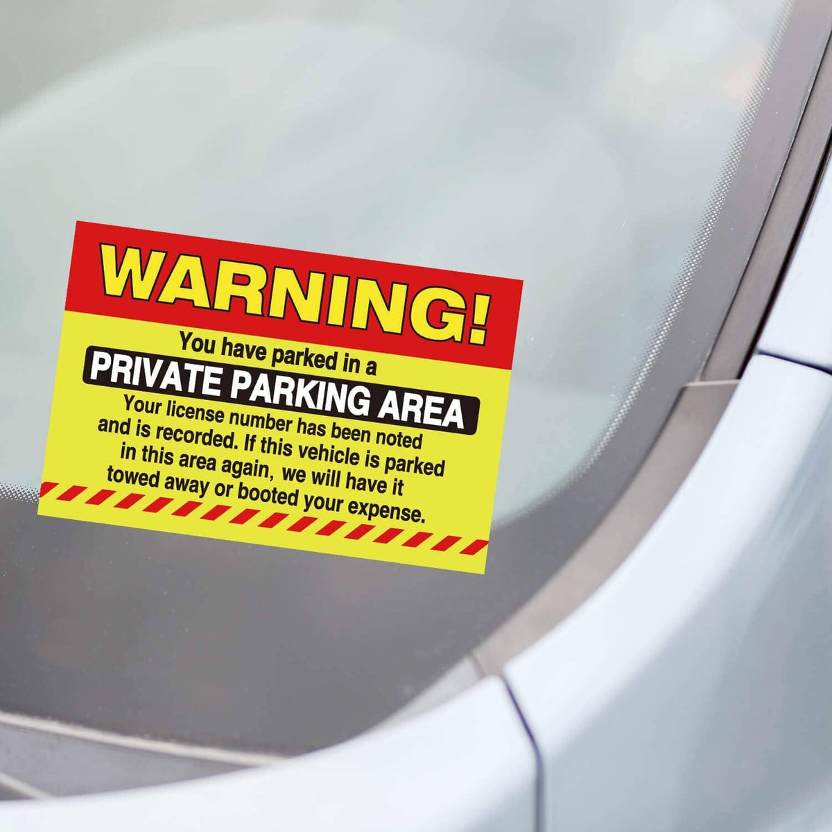 Private parking area warning sticker on car windshield, red and yellow notice