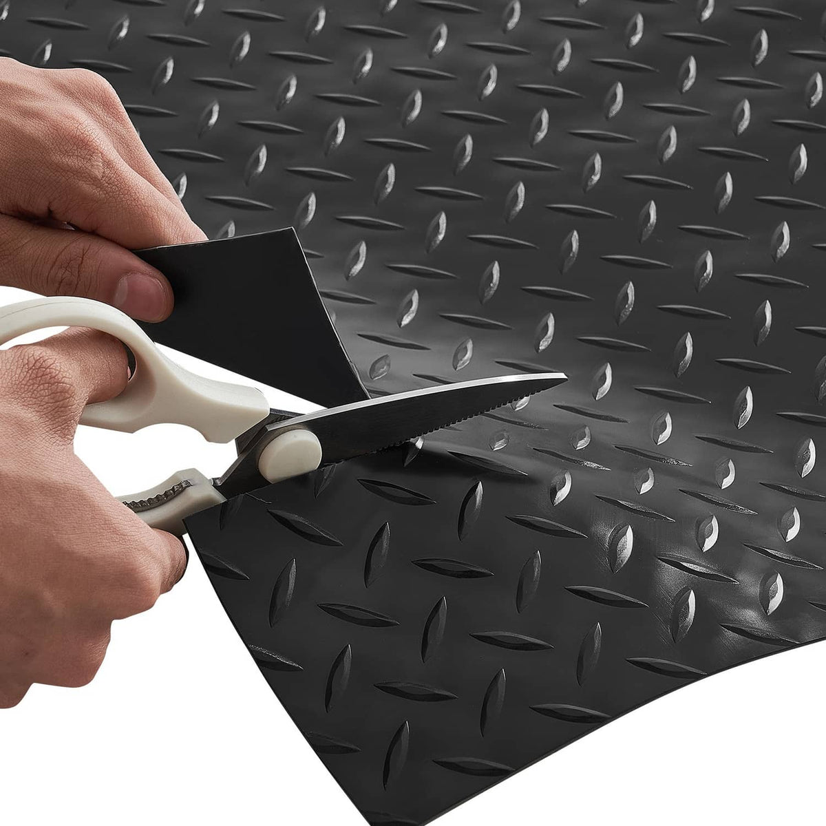 Black PVC garage floor mat being trimmed with scissors along the diamond texture