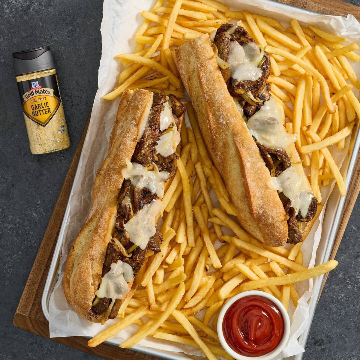 Garlic butter seasoning bottle beside loaded fries and cheese-topped sandwiches