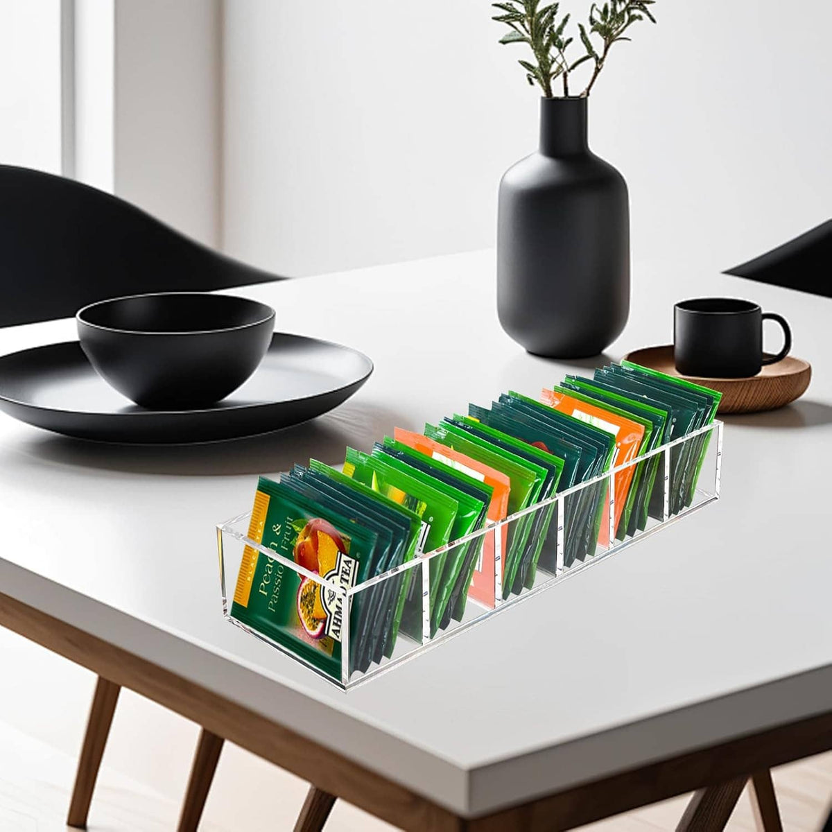 Clear acrylic tea bag organizer with slots holding green tea packets on a white table