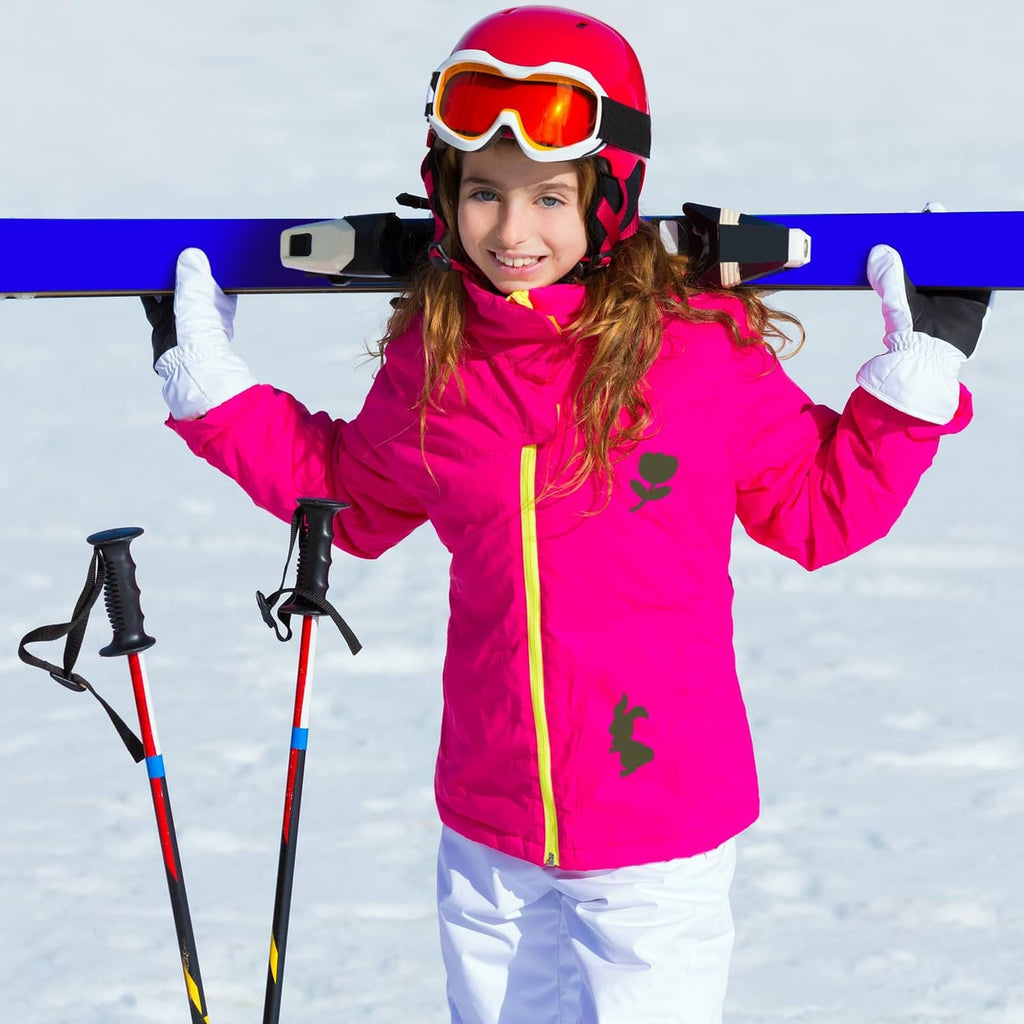 Girl in a bright pink ski jacket with goggles and helmet standing on snow