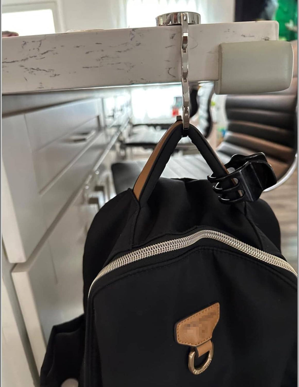 Foldable purse hook clamped to table edge; holds black handbag with top handle