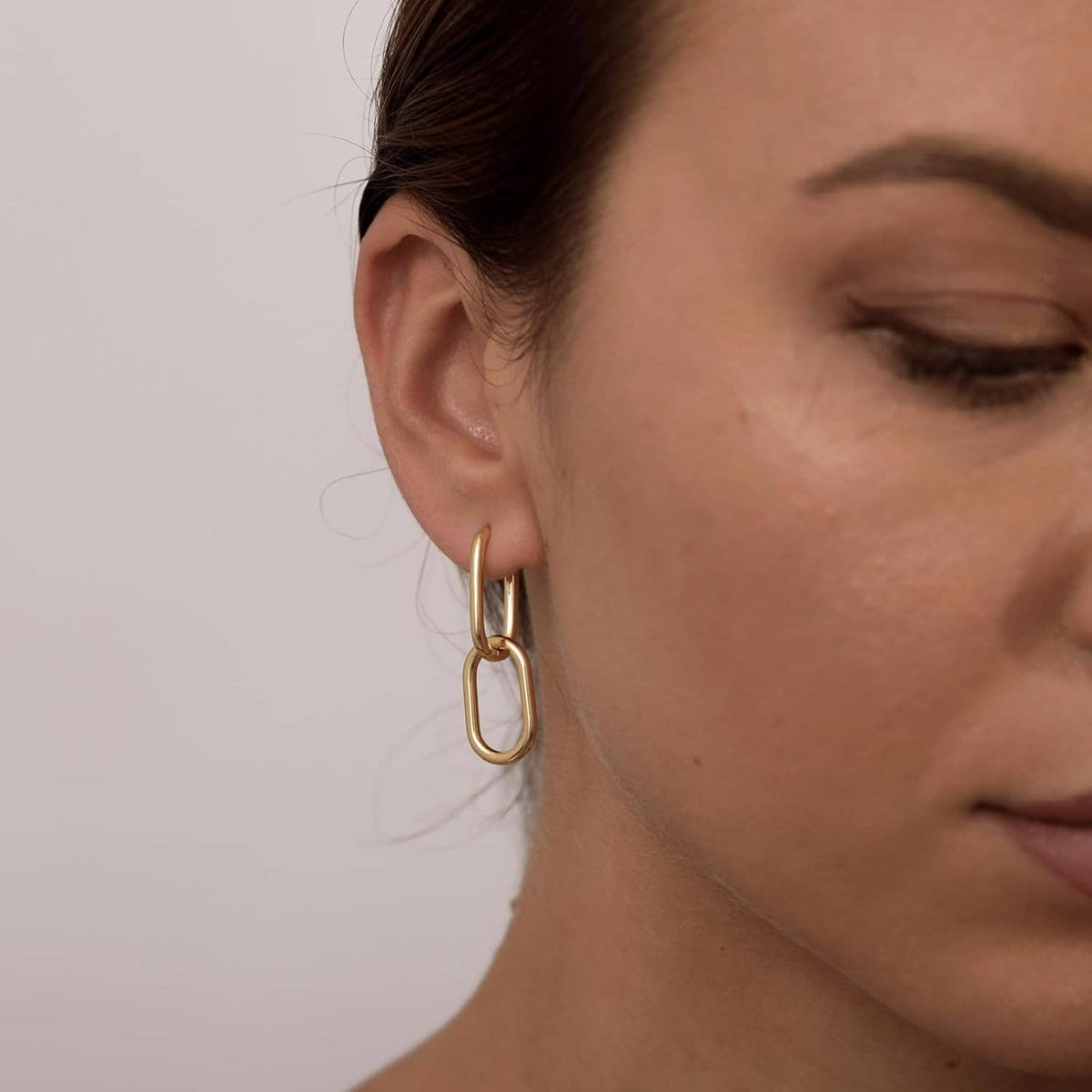 Gold paperclip huggie hoop earring with rectangular link, worn on ear