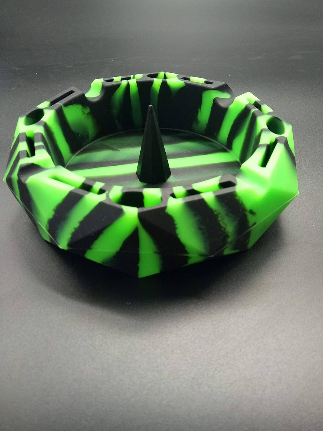 Neon green and black octagonal ashtray with central cone on smooth gray surface