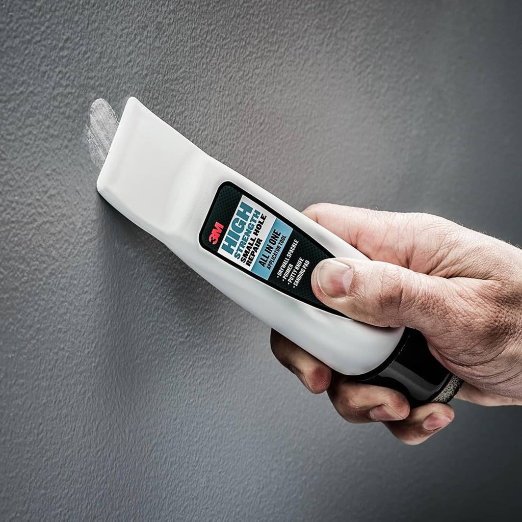 White repair applicator tool in hand spreading spackle over a small hole