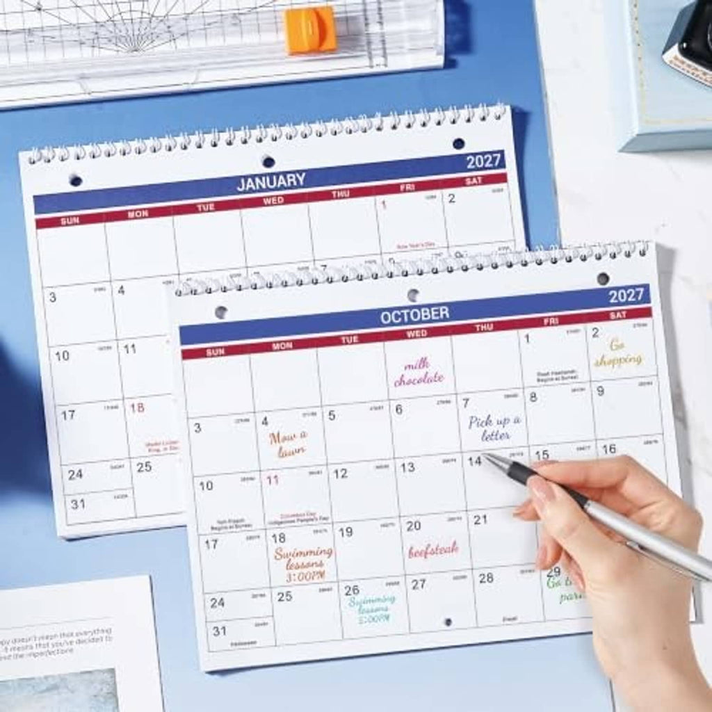Spiral-bound 2027 calendar pages for January and October with pen marking dates.