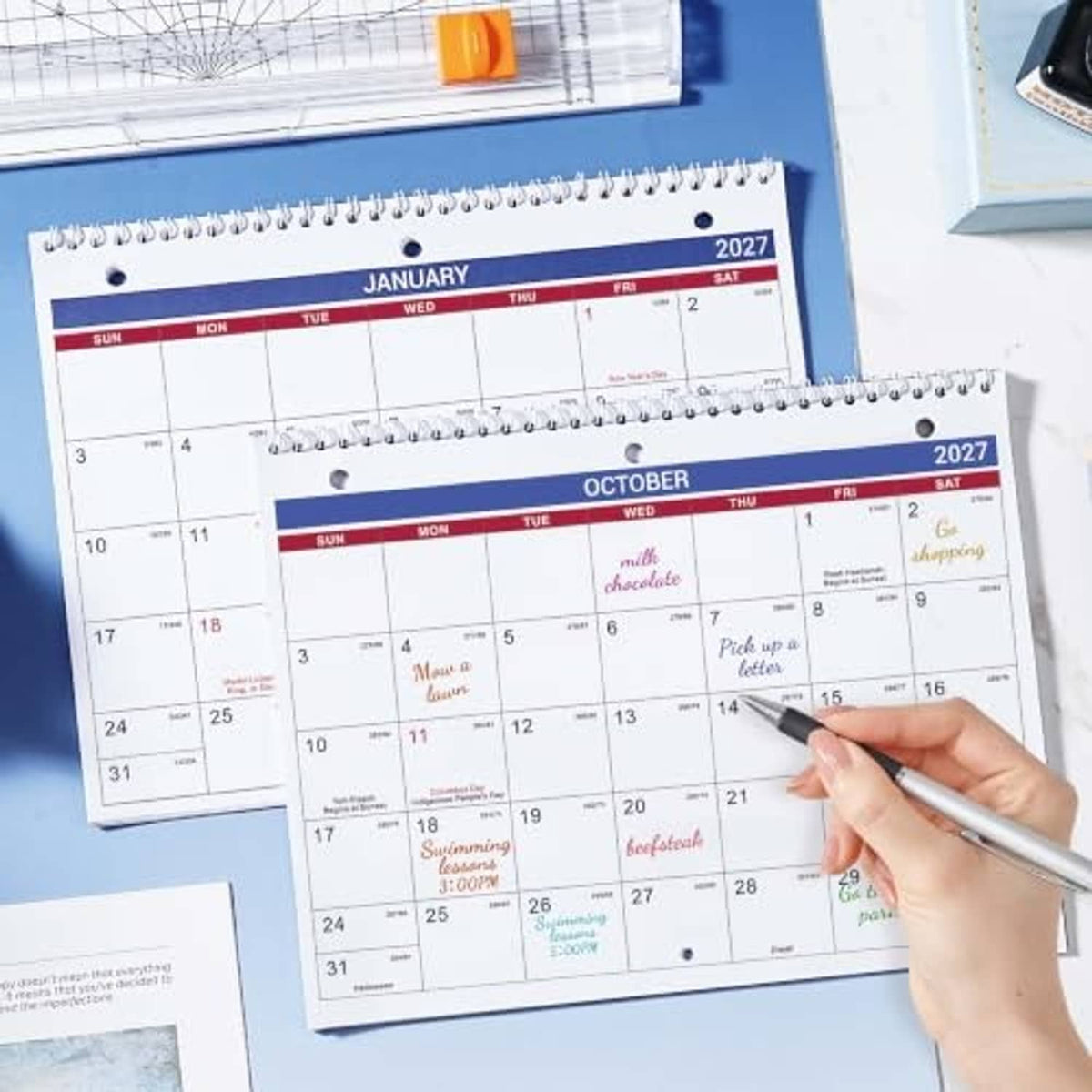 Spiral-bound 2027 calendar pages for January and October with pen marking dates.