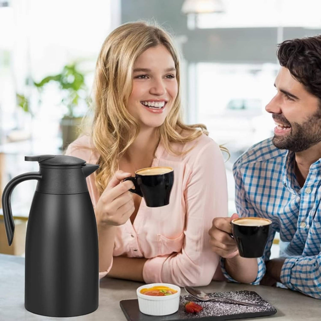 Black thermal coffee carafe on table with mugs and people holding drinks