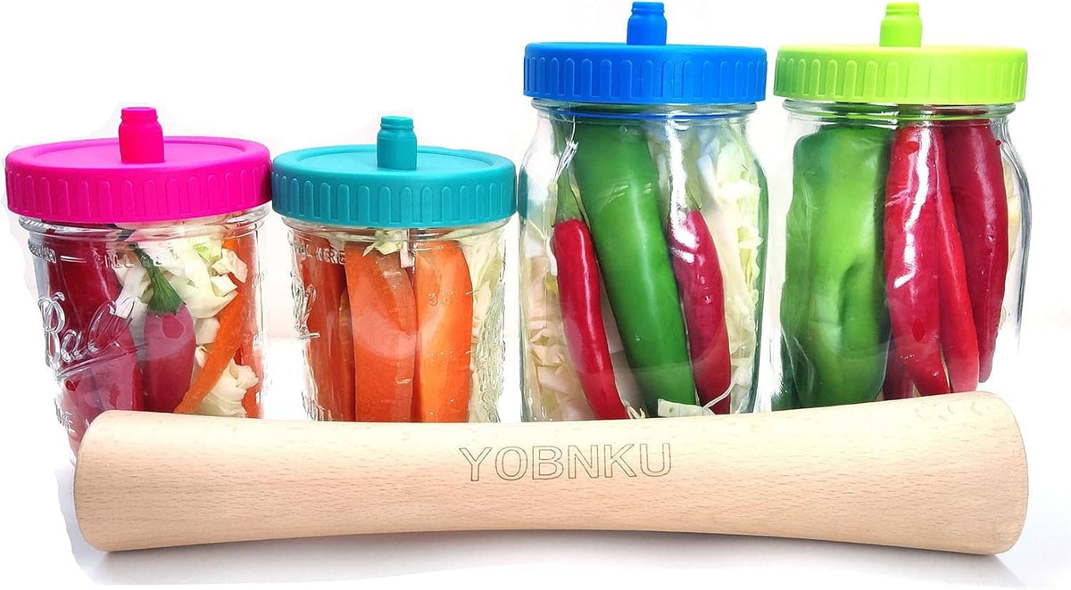 Fermentation jars with bright waterless airlock lids and vegetables, plus a wooden roller