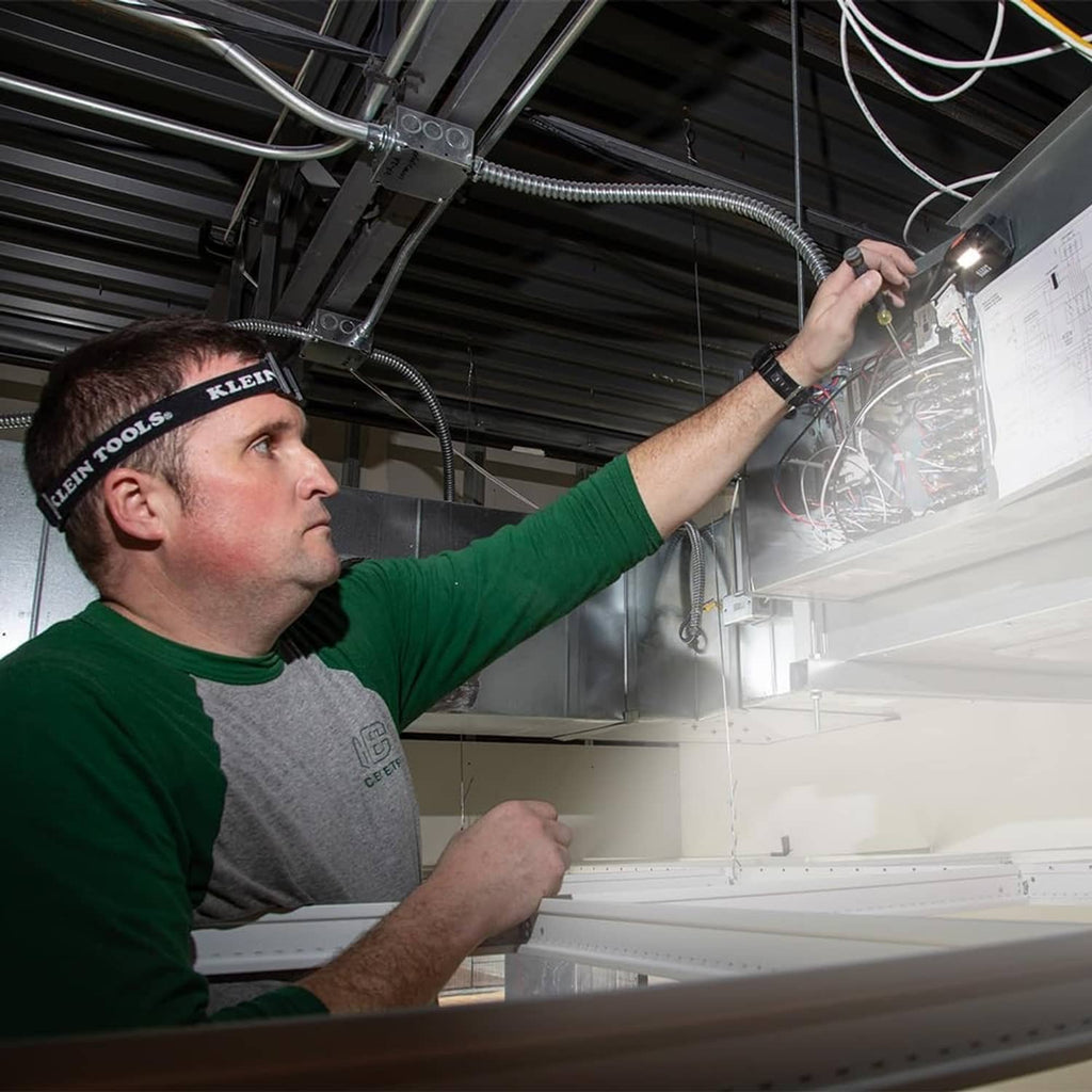 Worker using a rechargeable LED headlamp while pointing at overhead equipment