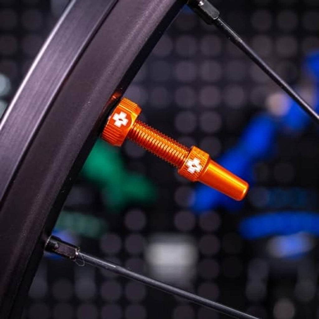 Orange Presta tubeless valve installed on a wheel rim, close-up view.