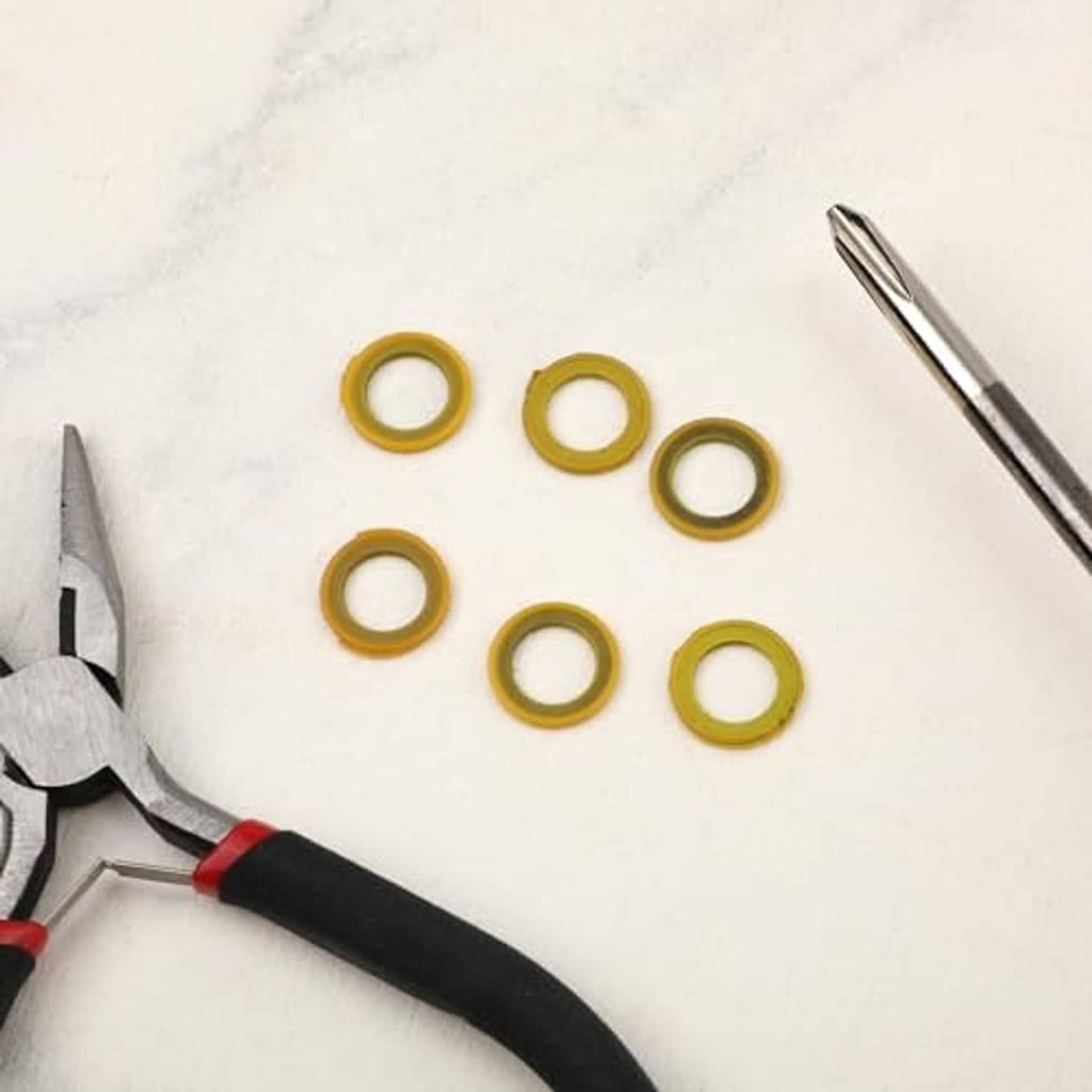 Set of six yellow round seal washers on white surface; tools in background