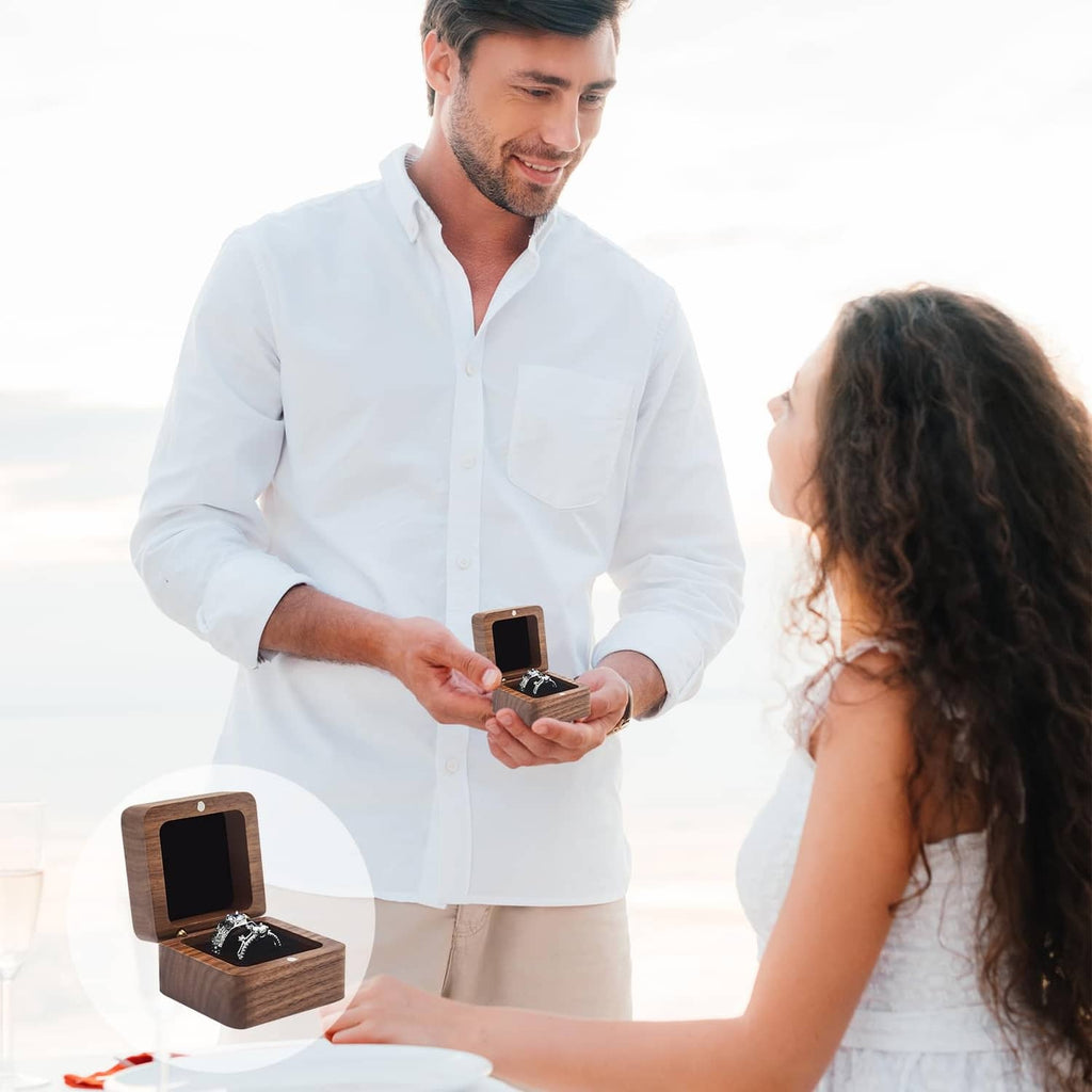 Man holding a dark wooden ring box with hinged lid open and black velvet ring pad