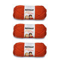 Three skeins of super bulky chunky yarn in solid orange, banded with labels