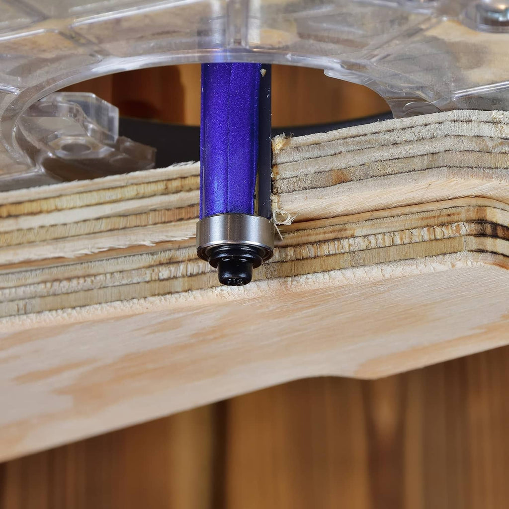 Close-up flush trim router bit with blue guide sliding along a wood edge
