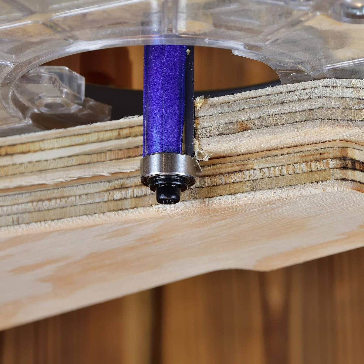 Close-up flush trim router bit with blue guide sliding along a wood edge