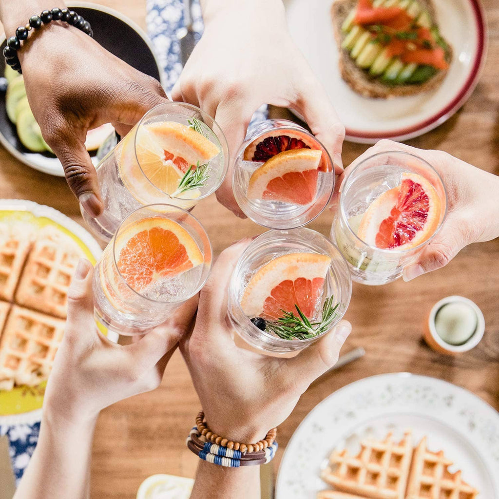 Group of small glasses of fruit-infused sparkling water held by hands
