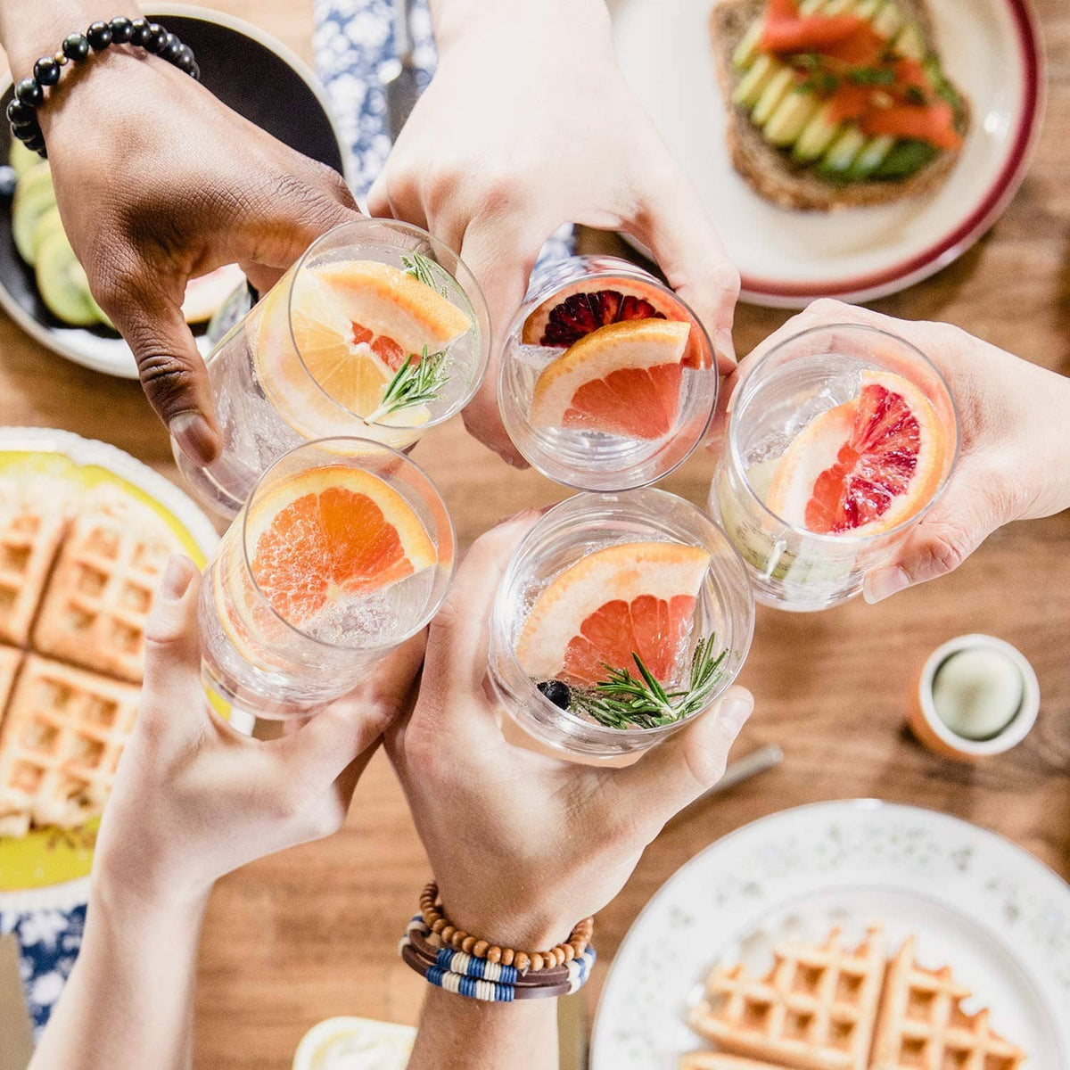 Group of small glasses of fruit-infused sparkling water held by hands