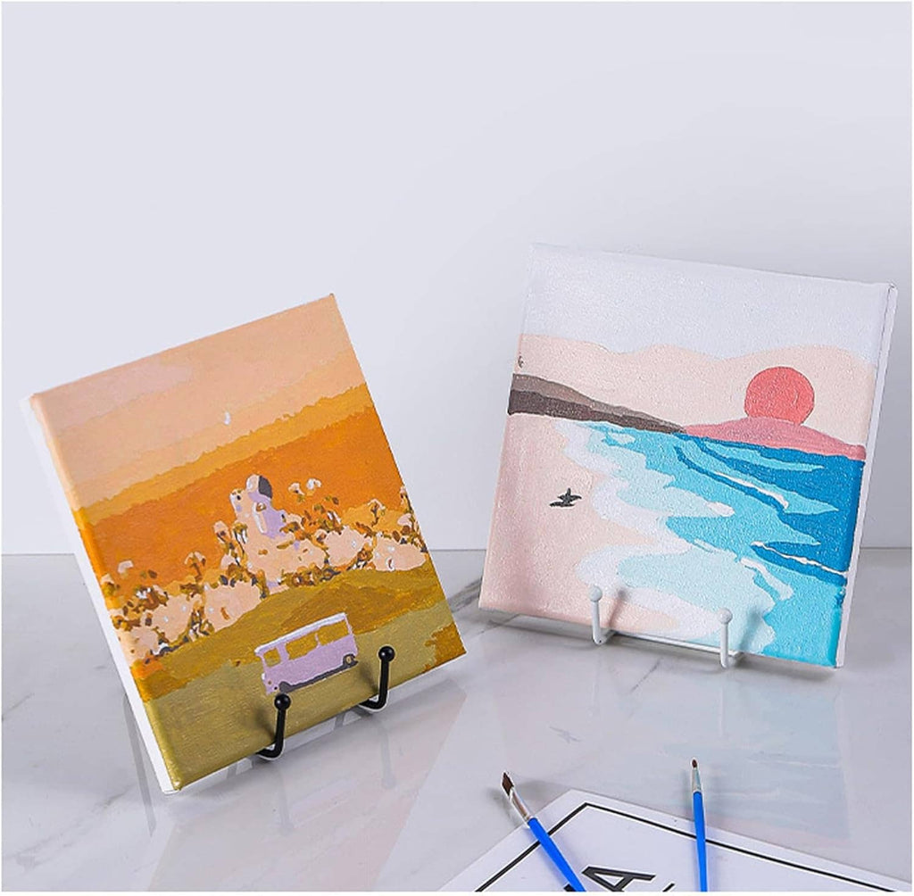 Black metal plate stands supporting two canvas artworks on a tabletop