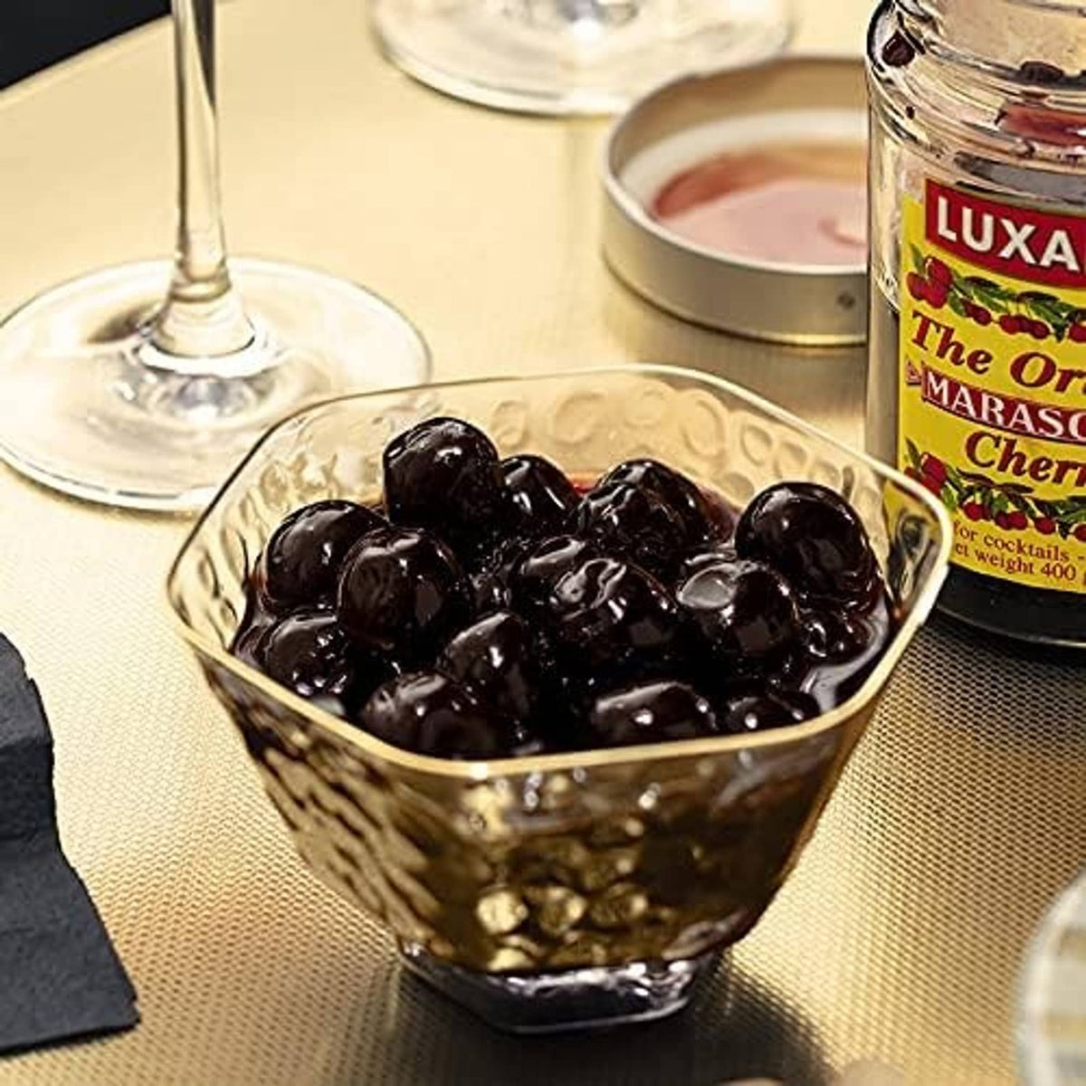 Glass bowl filled with dark maraschino cherries beside a jar for cocktails