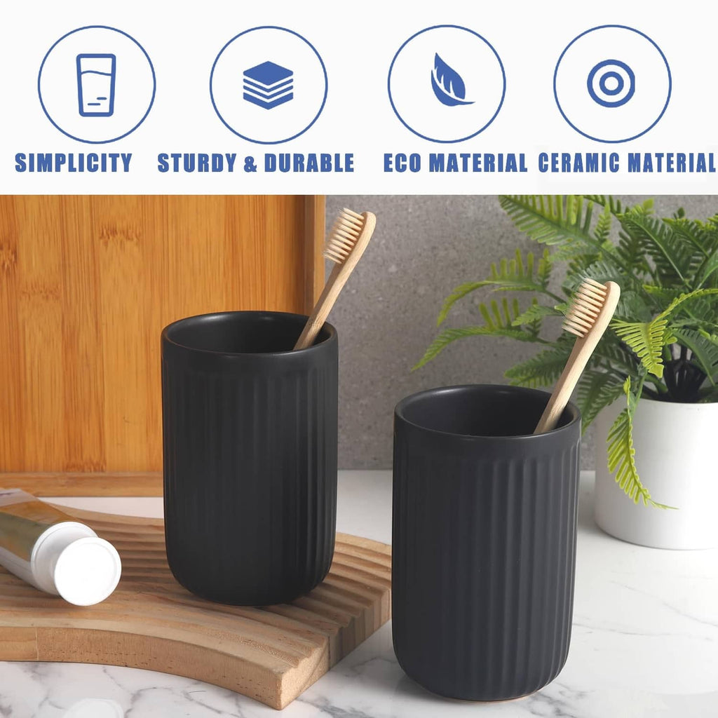 Two matte black ceramic toothbrush holder cups with ribbed sides and toothbrushes