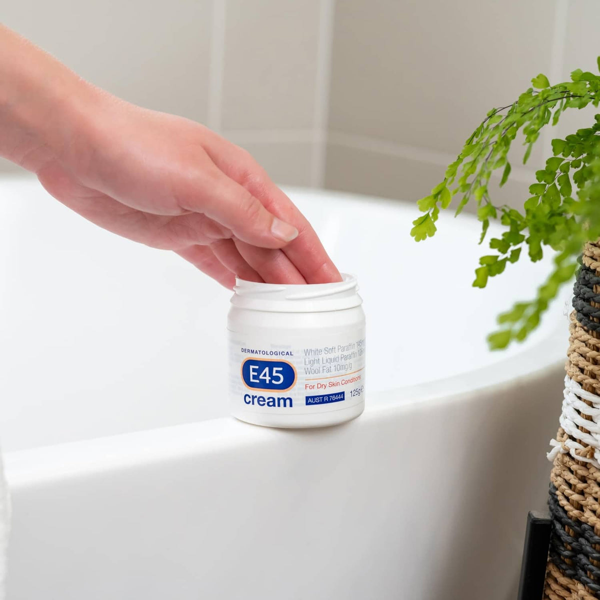 Hand placing E45 dermatological cream jar on bathroom sink