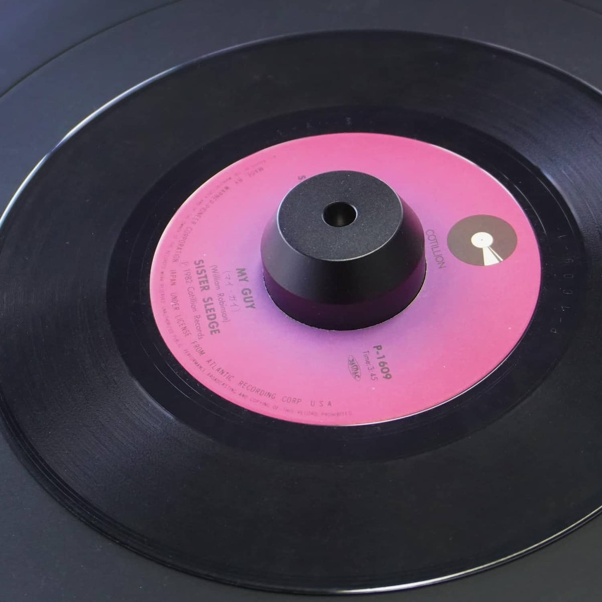 Black 45 RPM center adapter on a vinyl record with visible top center hole