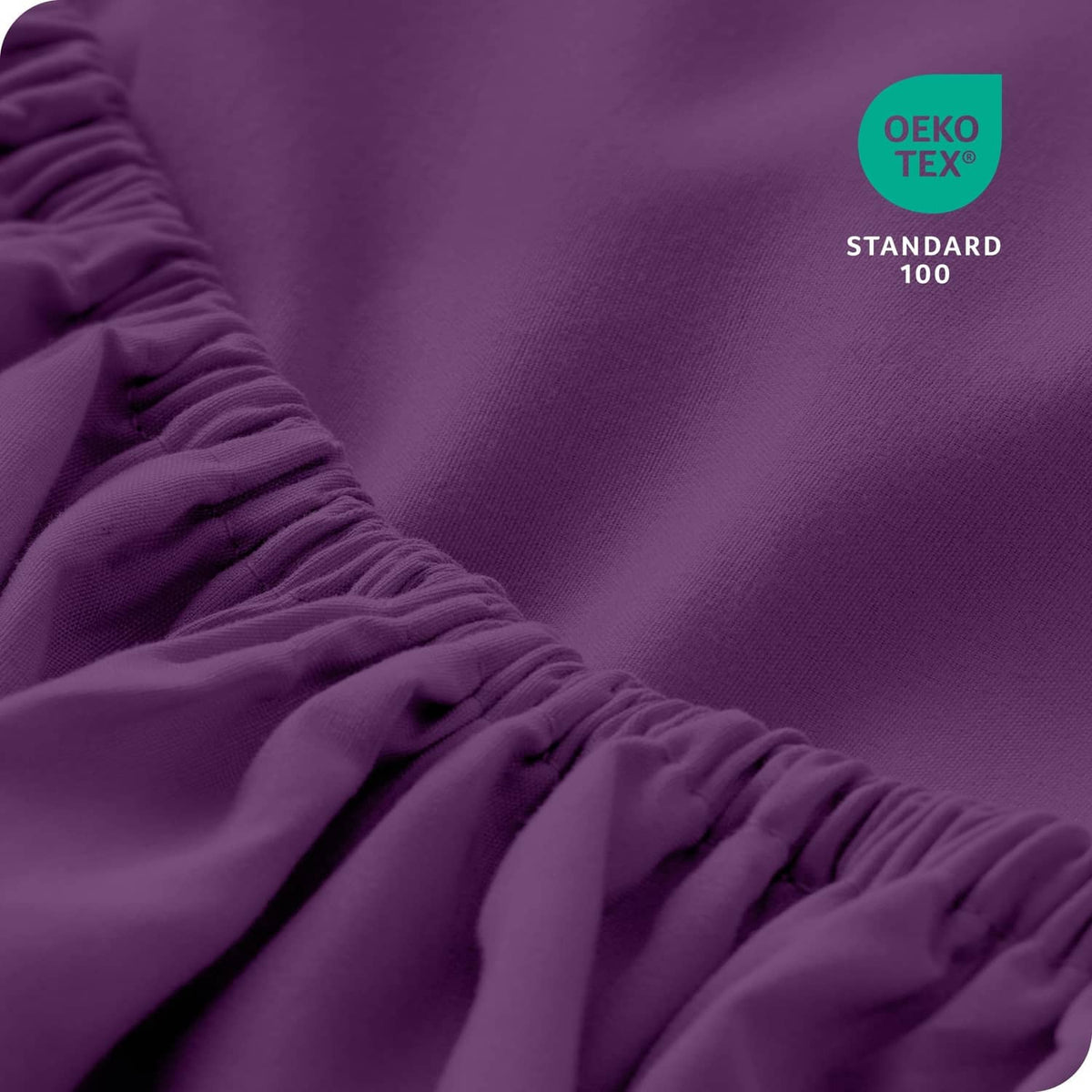 Purple fitted sheet close-up with ruched elastic edge and Oeko-Tex Standard 100 mark