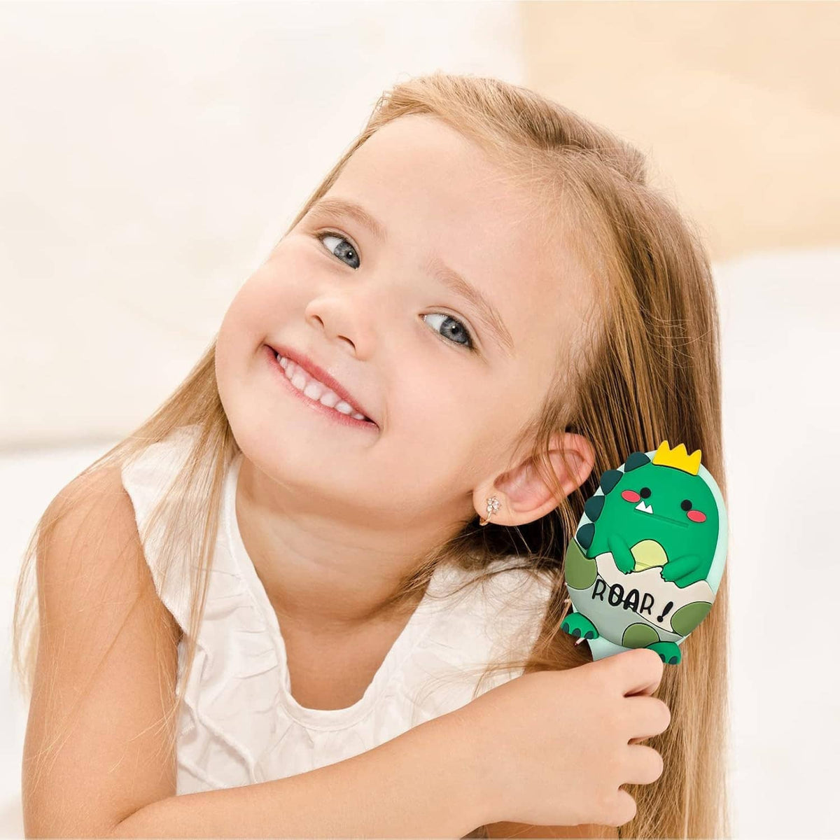 Mini kids hair brush with green dinosaur face on handle, child holding brush