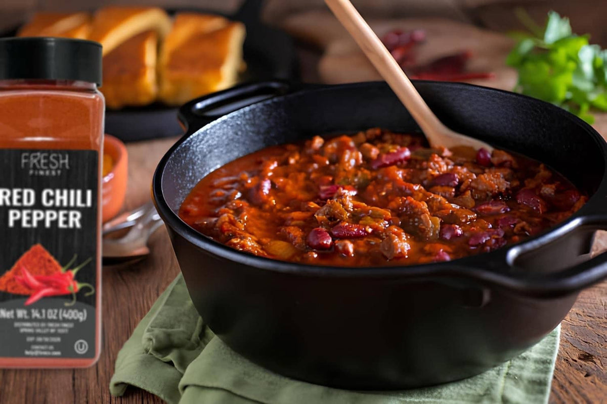 Red chili pepper seasoning jar next to chili in a black pot