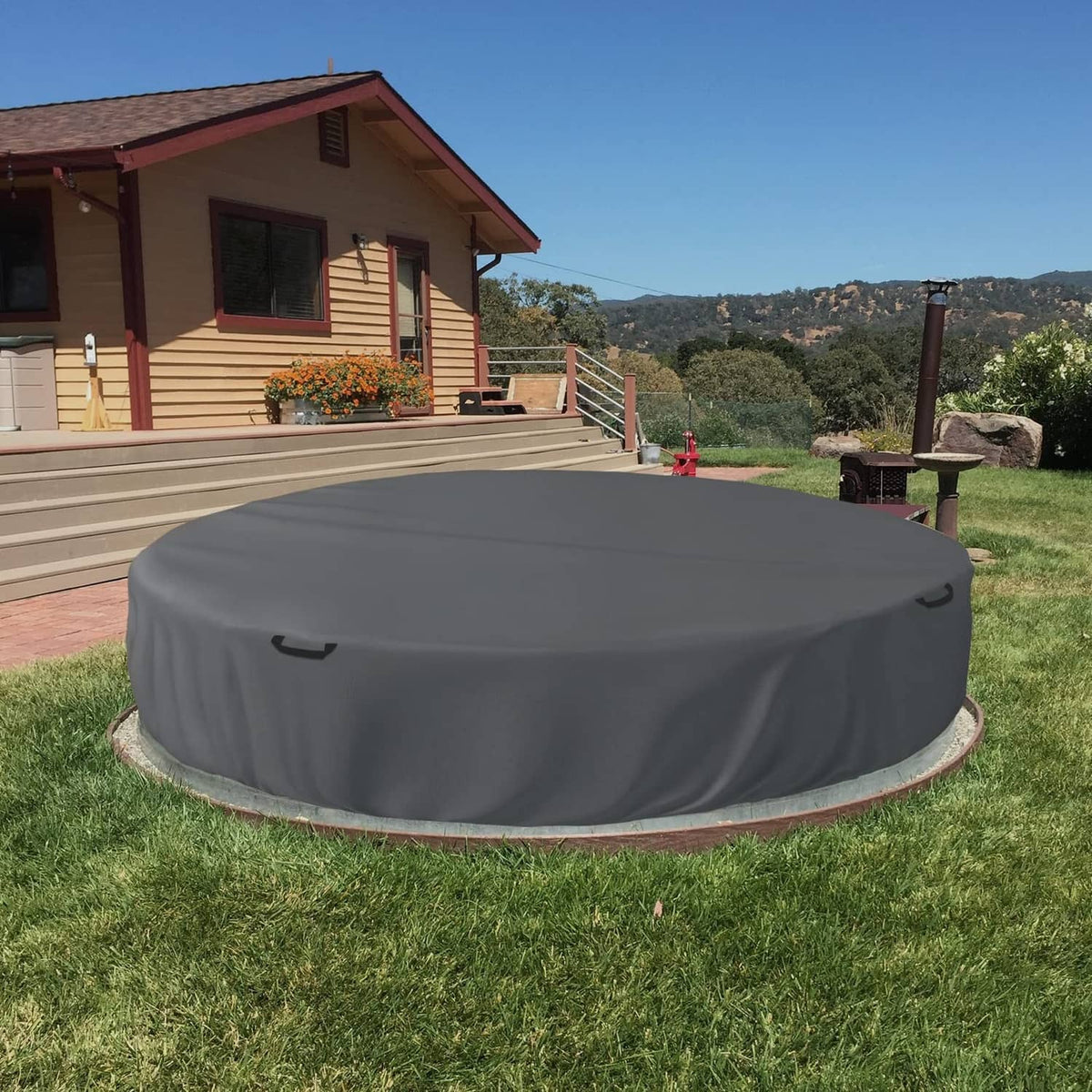 Grey round stock tank pool cover over outdoor pool with side strap loops.