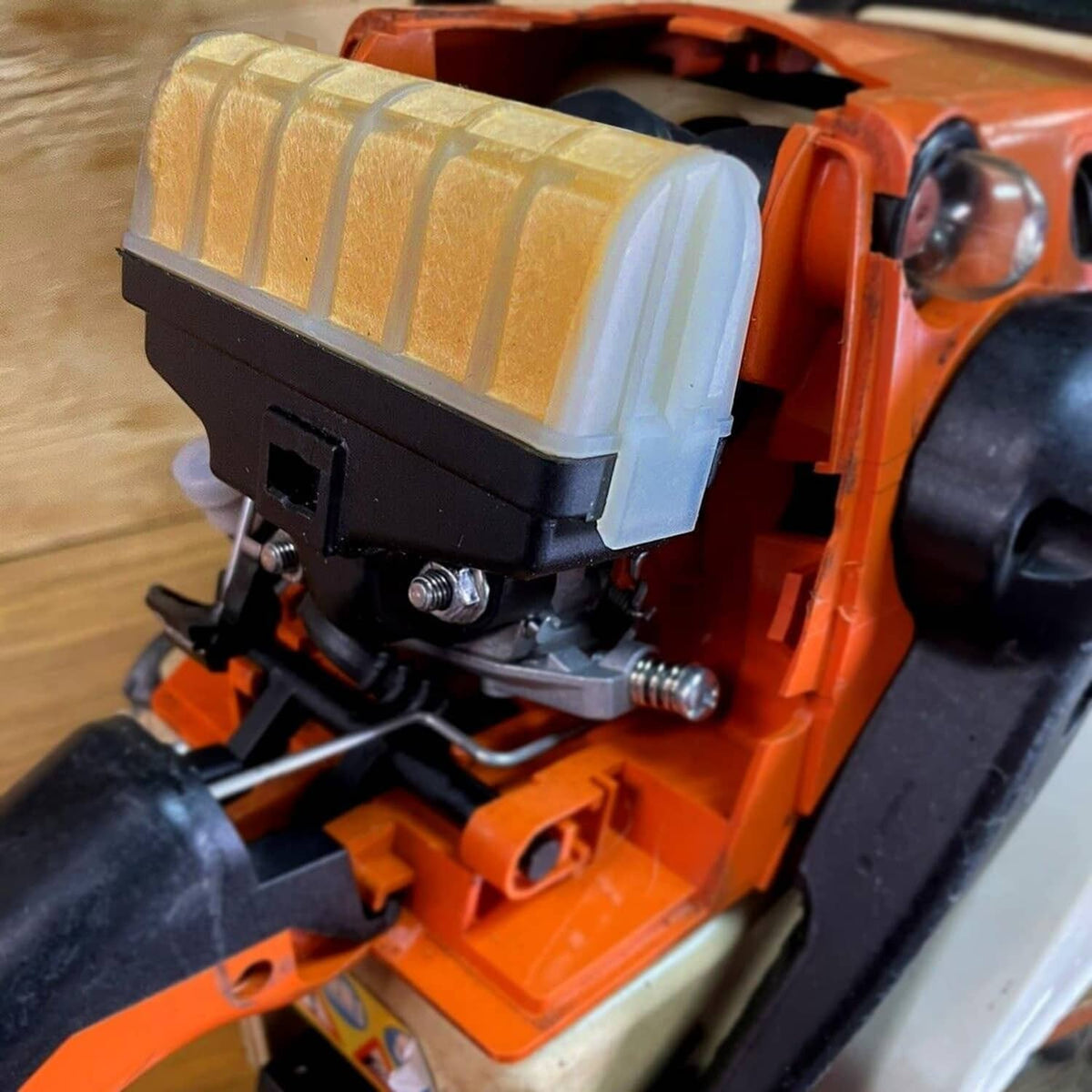 Close-up of tan air filter housing installed on an orange chainsaw engine.