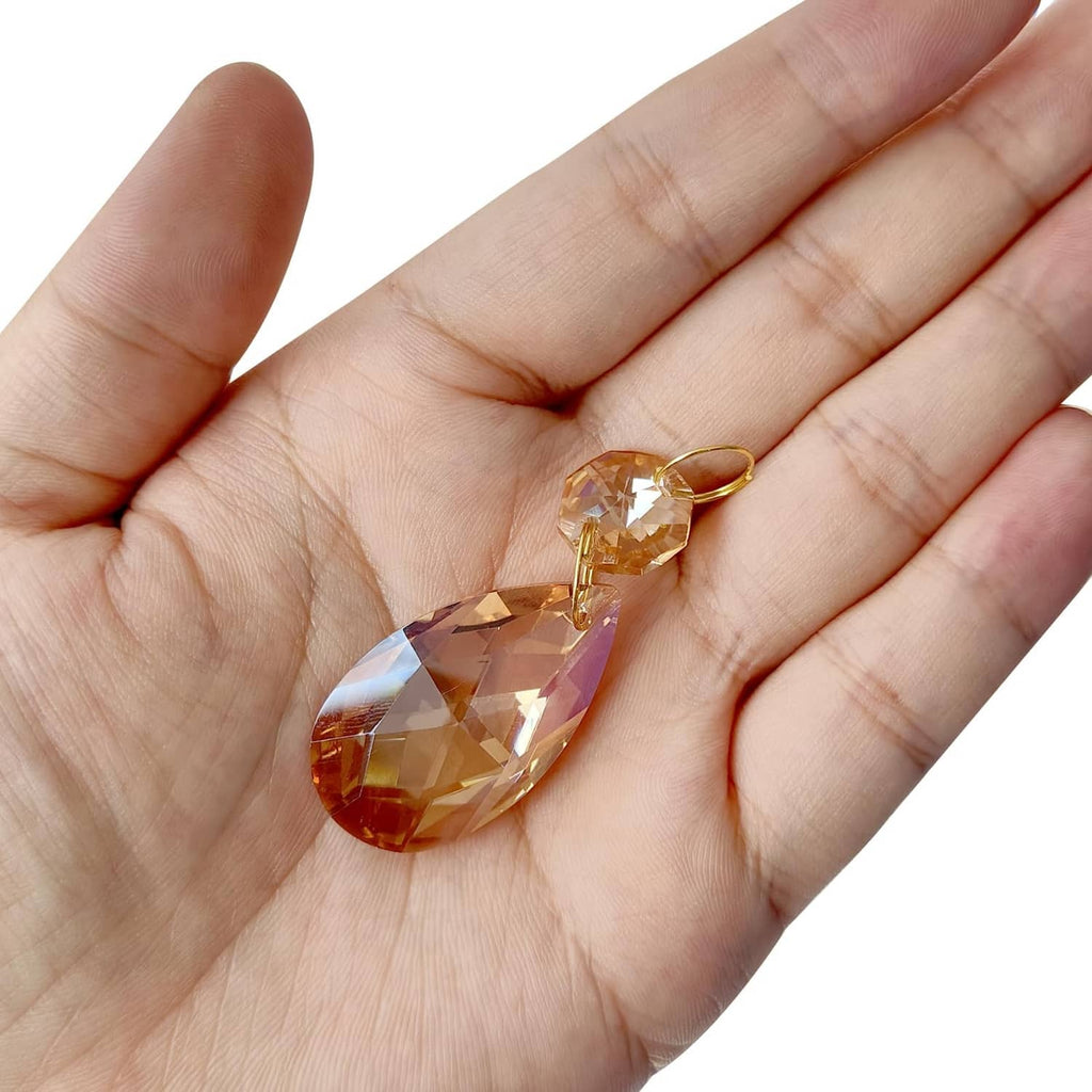 Amber teardrop crystal pendant bead with gold loop, shown in open palm