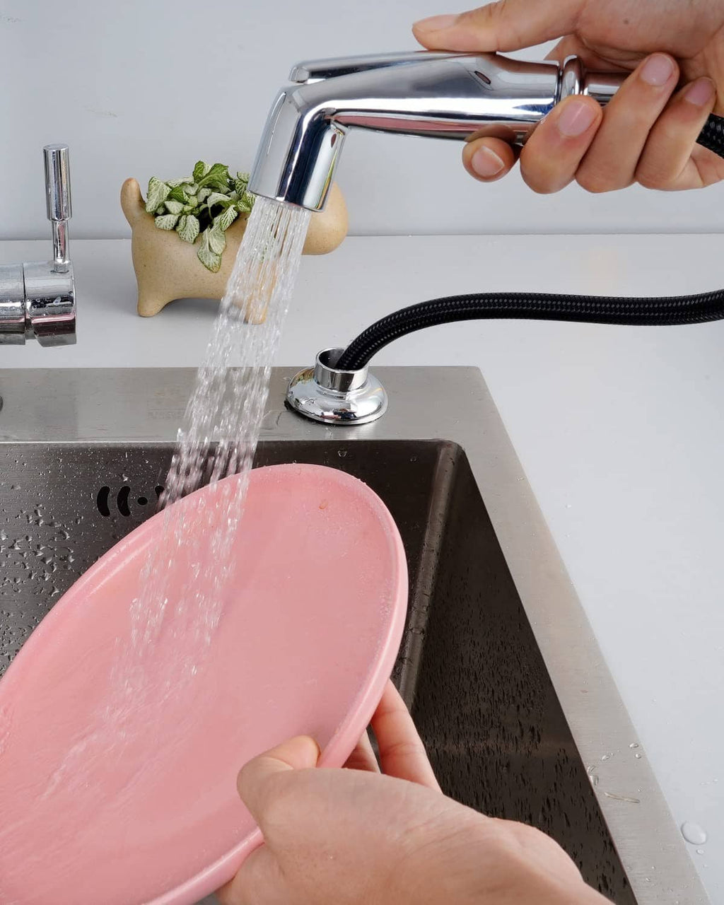 Chrome sink sprayer releasing water with black braided hose