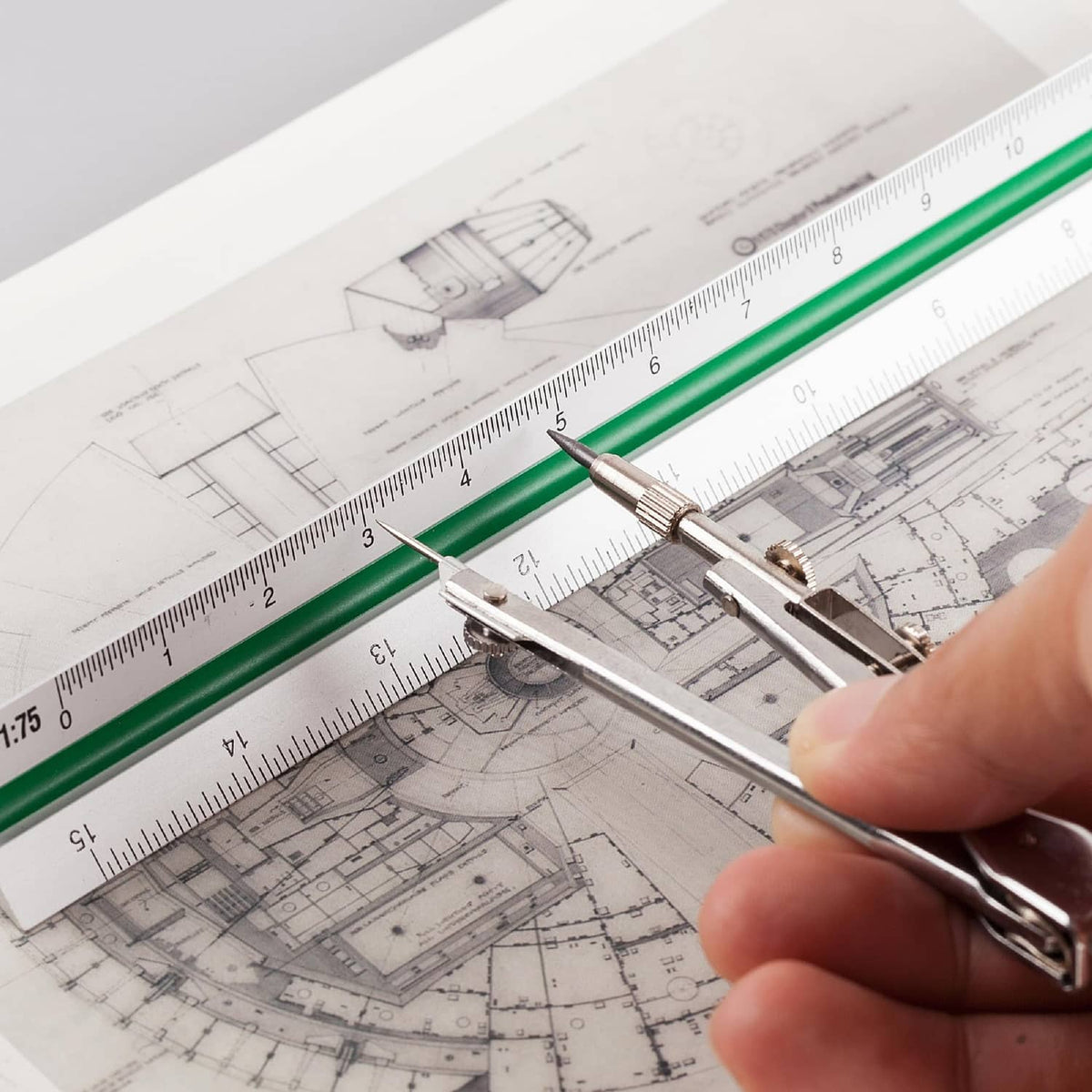 Architectural scale ruler with white body and green strip, used with a drafting compass tool