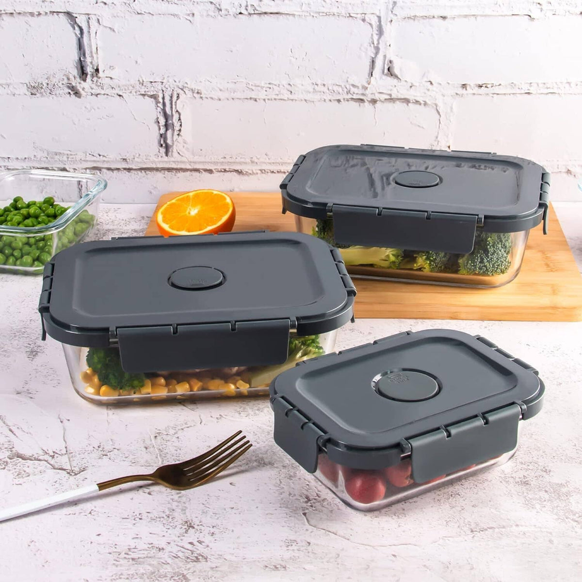 Three glass meal prep containers with dark gray lids, filled with vegetables and fruit